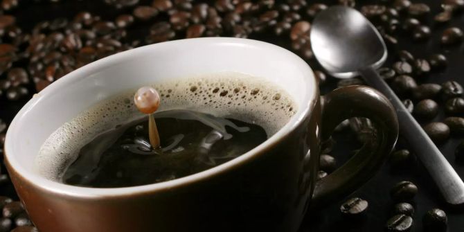 Tasse mit Kaffee und Löffel auf Kaffeebohnen, braun