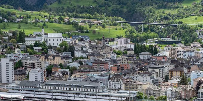 Blick auf Brig mit der A9 Simplonstrasse, der Kollegiumskirche, dem Stockalperpalast sowie der Iischi Arena und dem Bahnhof. brig