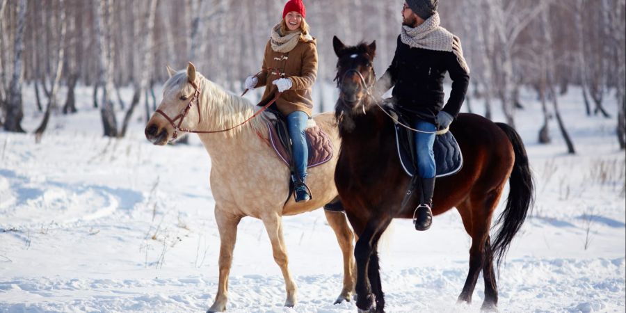 Zwei Personen reiten nebeneinander im Schnee.