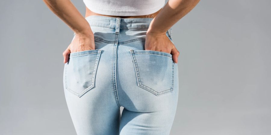 Abgeschnittene Ansicht einer jungen Frau in Jeans mit Händen in Taschen isoliert auf grau.