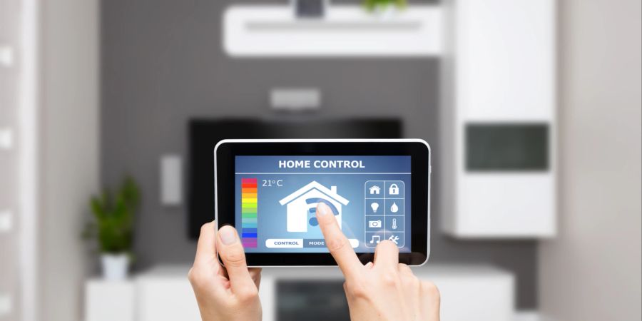 Ein Tablet in zwei Händen wird vor eine Wohnzimmerwand gehalten. Darauf sind Temperaturregler zu erkennen.