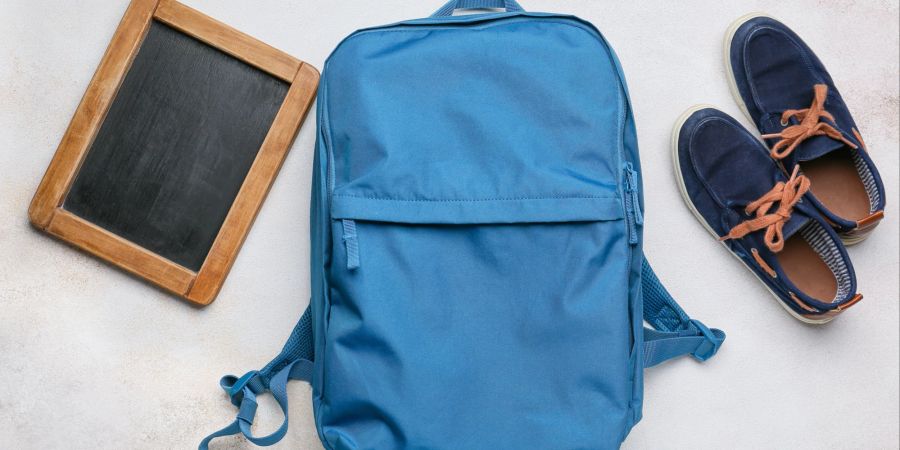 Schulrucksack, Schuhe und Tafel auf hellem Hintergrund.