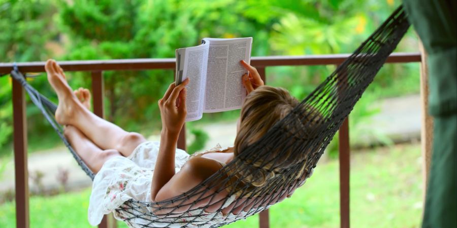 Frau liest Buch in Hängematte.