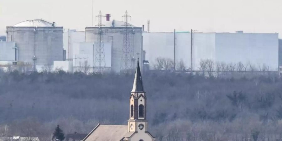 Der Kirchturm der katholischen Kirche St. Peter und Paul in deutschen Hartheim am Rhein ist vor dem Atomkraftwerk Fessenheim auf der französischen Seite der Grenze zu sehen. Foto: Patrick Seeger/dpa