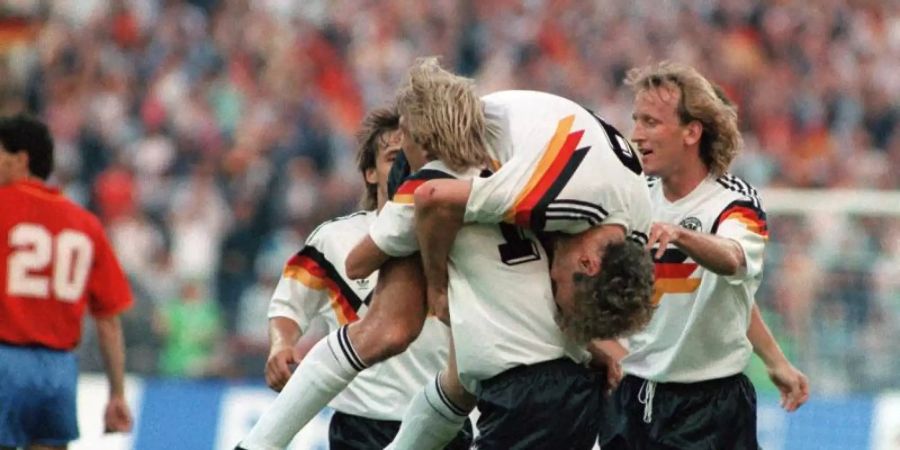 Wurden 1990 zusammen Weltmeister: Jürgen Klinsmann (M, vorn) schultert vor Freude Rudi Völler (M, oben). Foto: dpa/dpa/Archiv/dpa