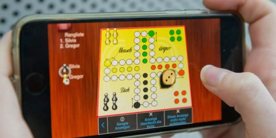 Eine Frau spielt «Mensch ärgere Dich nicht» auf einem Smartphone. Foto: picture alliance / dpa