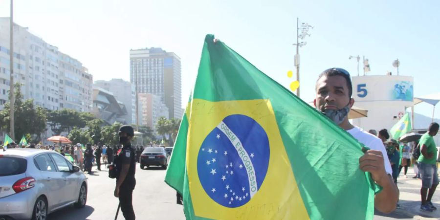 Ein Unterstützer des brasilianischen Präsidenten Bolsonaro hält bei einem Protest an der Copacabana eine brasilianische Fahne hoch. Foto: Fausto Maia/TheNEWS2 via ZUMA Wire/dpa