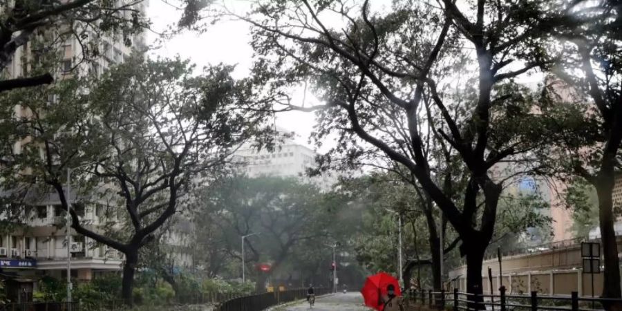 Ein Mann mit einem Regenschirm geht über eine Strasse in Mumbai, auf der vom Wind abgerissene Äste und Blätter liegen. Foto: Rajanish Kakade/AP/dpa