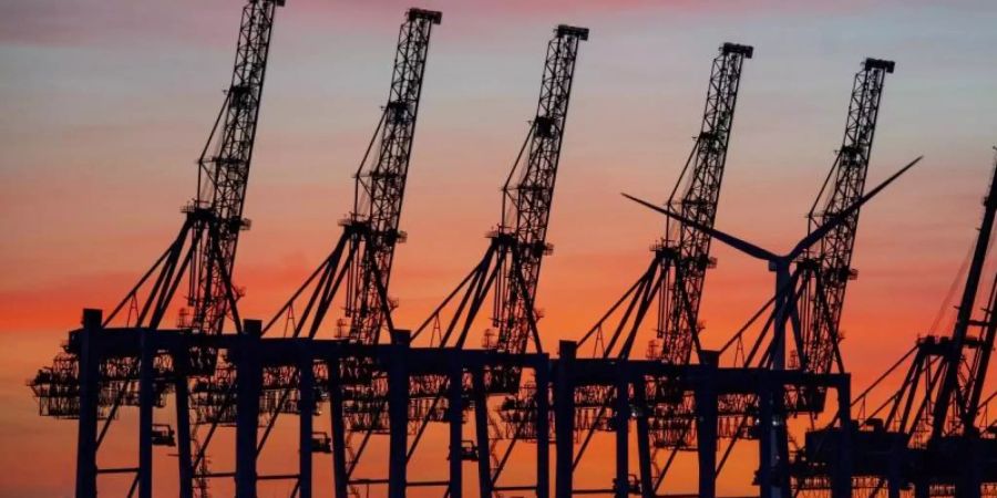 Die Sonne geht hinter den hochgeklappten Containerbrückenkränen, die normalerweise Schiffe entladen, im Hamburger Hafen unter. Foto: Axel Heimken/dpa