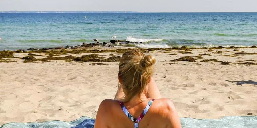 Eine Urlauberin geniesst das sommerliche Wetter am Ostseeufer in Timmendorfer Strand. Foto: Ulrich Perrey/dpa