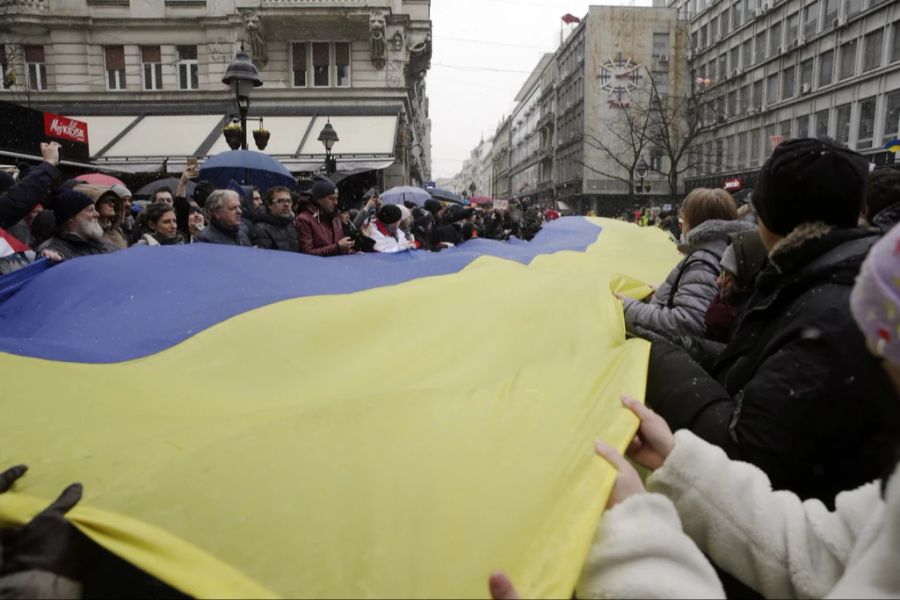 Demonstrierende in Belgrad halten eine ukrainische Flagge.