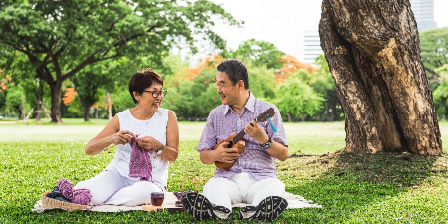 asiatisches pärchen im park, ukulele - mann, frau häkelt