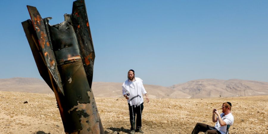 Israelische ultraorthodoxe jüdische Männer inspizieren das Wrack einer Rakete, die nach einem iranischen Angriff nahe der Stadt Jericho im Westjordanland aus dem Boden ragt. Foto: Jam...
