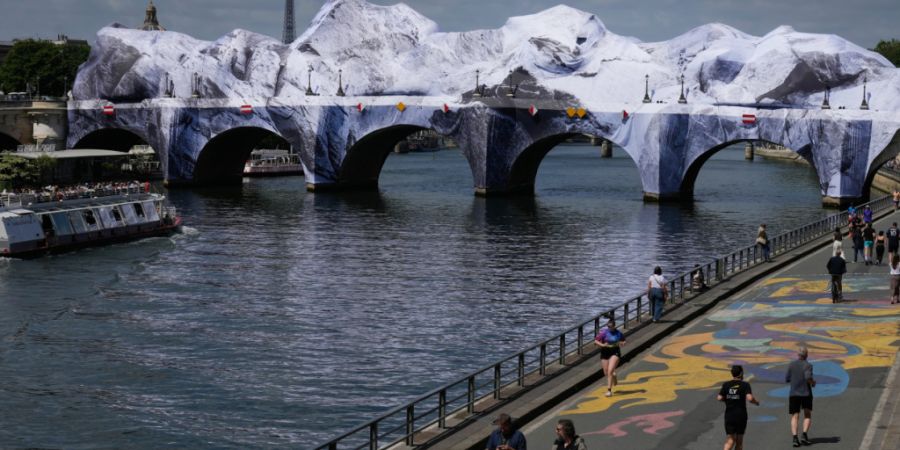 Menschen spazieren entlang der Seine neben «The Pont Neuf Cave», einer aufgeblasenen Kunstinstallation des französischen Straßenkünstlers JR. Foto: Michel Euler/AP/dpa - ACHTUNG: Nur...