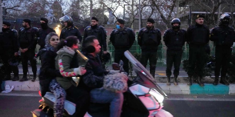 Polizisten schützen die britische Botschaft während einer Demonstration von Hardliner-Anhängern der iranischen Regierung, während Menschen auf ihrem Motorrad an den Einsatzkräften ...