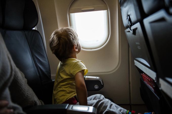 Kinder, die besonders empfänglich für die Stimmung ihrer Umgebung sind, können gerade in fremdem Umfeld schnell überfordert sein. Kind im Flugzeug schaut aus dem Fenster