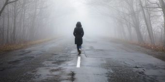 Frau spaziert alleine auf eienr Strasse im Nebel.