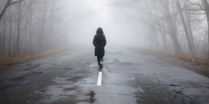 Frau spaziert alleine auf eienr Strasse im Nebel.