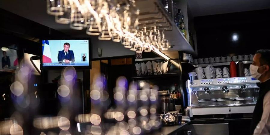 Ein Barkeeper schaut sich die Fernsehansprache von Präsident Macron in einem Café in Marseille an. Foto: Christophe Simon/AFP/dpa