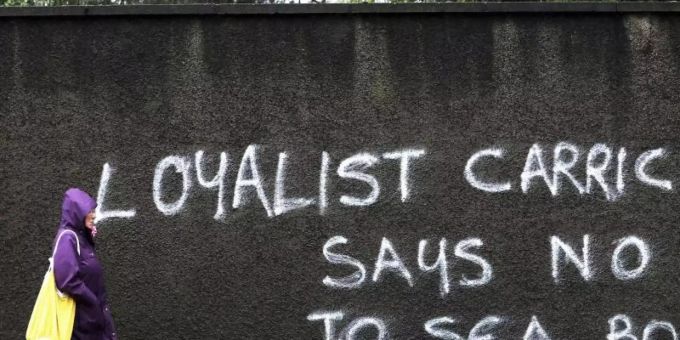 A passer-by walks past a graffiti in Belfast that reads “Loyalist Carrick says no to Sea Border”.  Photo: Peter Morrison / AP / dpa