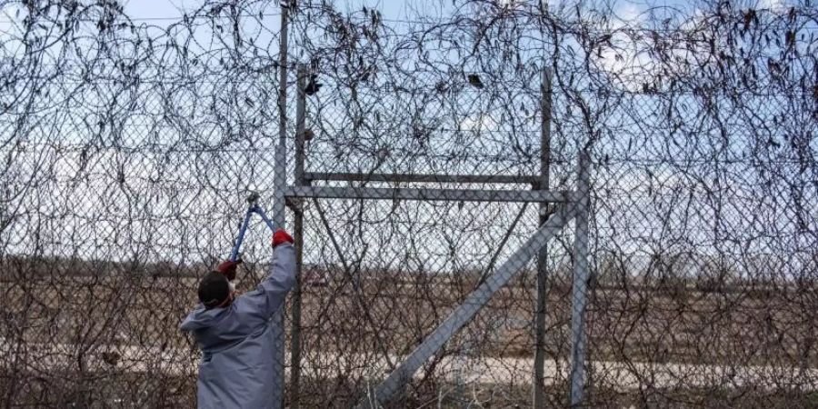 Ein Migrant versucht an der türkisch-griechischen Grenze, mit einer Drahtschere den Zaun durchzuschneiden. Foto: Yasin Akgul/dpa