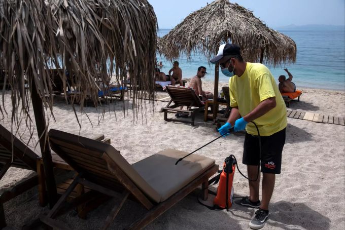 Ein Mitarbeiter mit Mundschutz desinfiziert einen Liegestuhl am Strand von Alimos in der Nähe von Athen. Coronavirus - Griechenland