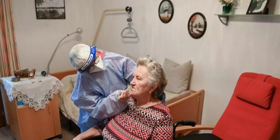 Die Krankenschwester eines mobilen Test-Teams des Deutschen Roten Kreuzes (DRK) testet in einer DRK-Seniorenbetreuungseinrichtung in Brandenburg eine Seniorin. Foto: Jens Kalaene/dpa-Zentralbidl/dpa