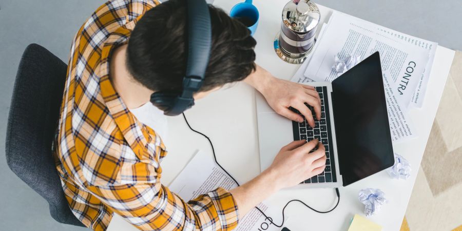 Junger Mann arbeitet am Laptop mit Kopfhörer