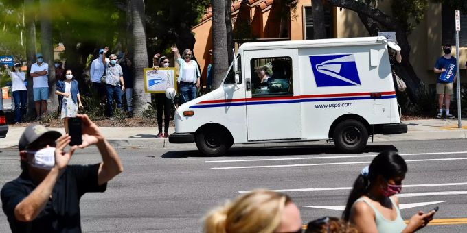 Postwagen fahren an Demonstranten vorbei, die an einer Kundgebung gegen die finanziellen Einschnitte bei dem United States Postal Service (USPS) teilnehmen. Trotz eines Einlenkens von Post-Chef DeJoy geht der Streit um die Briefwahl und Ausstattung der US-Behörde vor der Präsidentschaftswahl im November weiter. post briefwahl