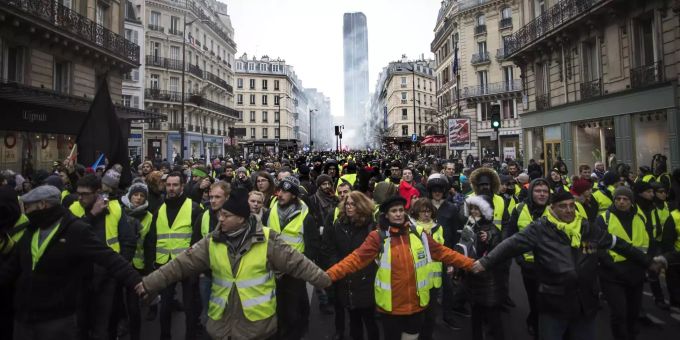«Macron tritt zurück», fordern die «Gelbwesten». «Gelbwesten» halten sich während einer Demonstration an den Händen.
