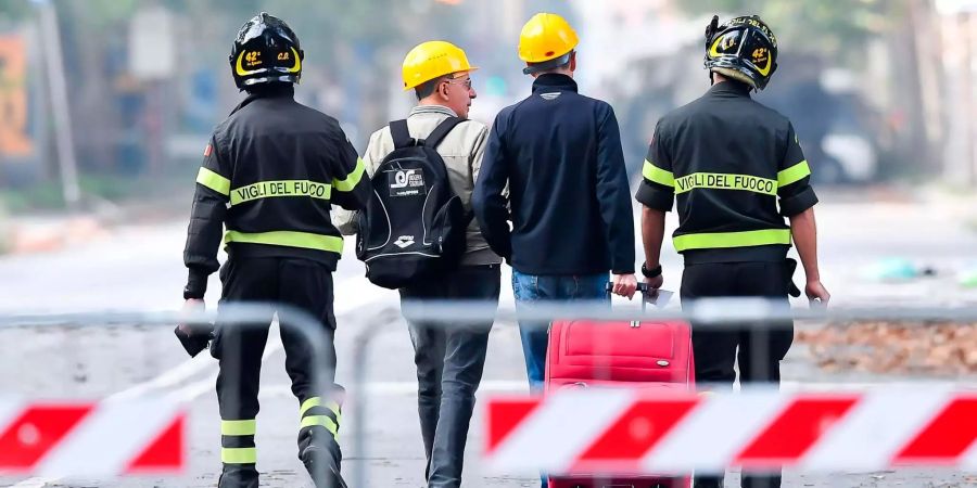 Feuerwehrleute begleiten Anwohner zu ihrem evakuierten Haus unter der eingestürzten Morandi-Brücke.