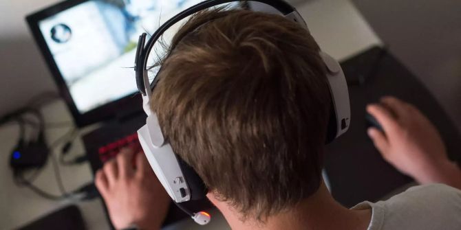 Ein junger Mann sitzt  mit einem Headset vor einem Laptop und spielt ein Online-Computerspiel.