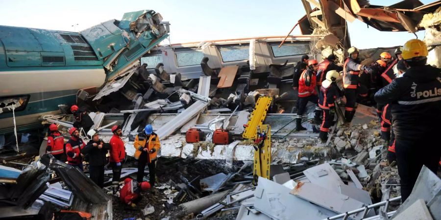 Rettungsdienstmitarbeiter stehen inmitten der Trümmer eines entgleisten Zuges.