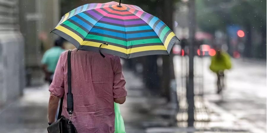 Ein Mann mit einem Schirm läuft im Regen.