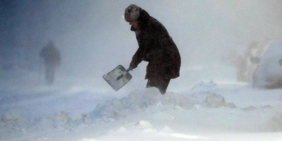 Eine Frau schaufelt in Boston durch den Schnee einen Weg zu ihrem Auto frei.