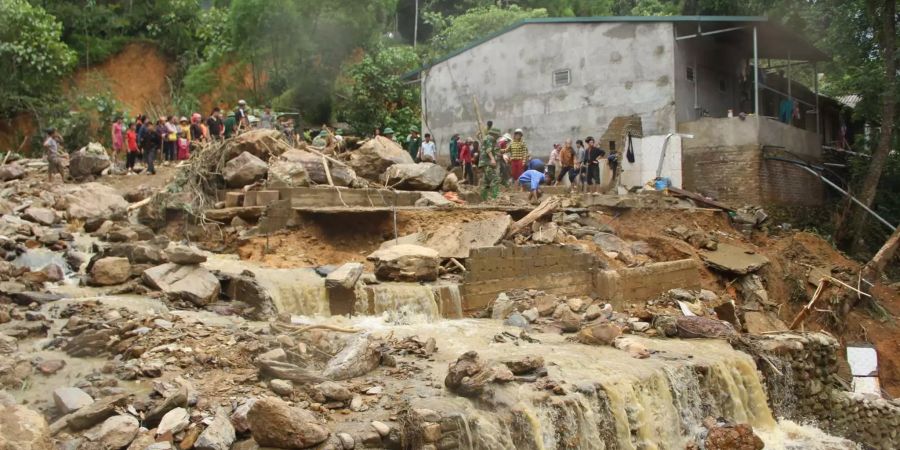 Dorfbewohner in Vietnam stehen vor den Überresten eines Hauses, das von einer Sturzflut mitgerissen wurde.