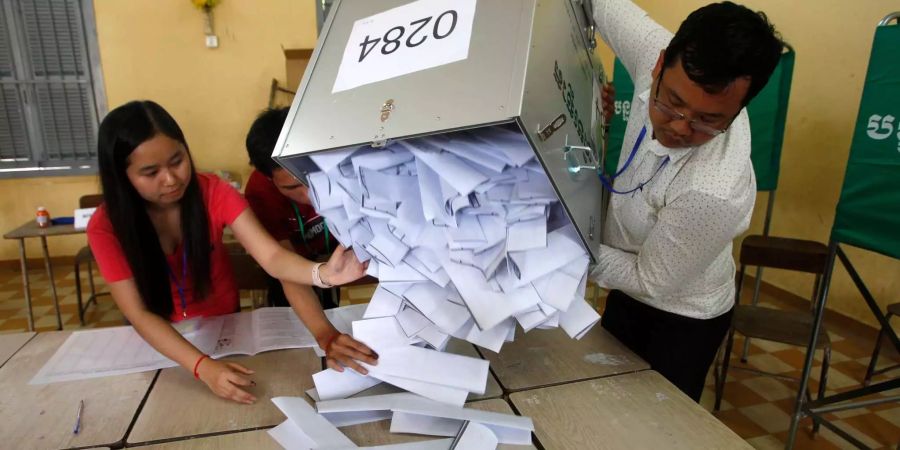 Wahlhelfer leeren eine Wahlurne, bevor sie mit dem Auszählen der Stimmen beginnen. In Kambodscha hat am Sonntag die umstrittene Parlamentswahl begonnen.