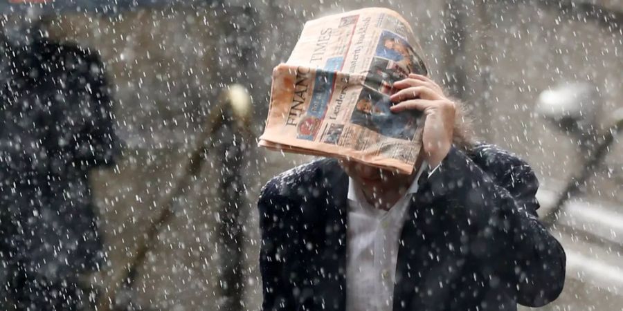 Ein Mann in London schützt sich mit einer Zeitung gegen den Regen.