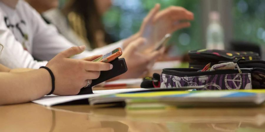 Schüler sitzen mit Handy an ihrem Platz in der Schule - Keystone