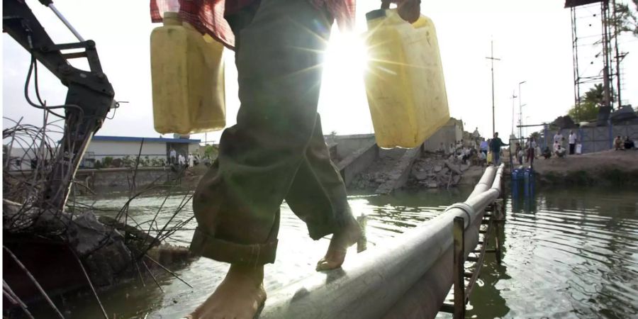 Ein irakischer Junge trägt zwei Plastikkanister während er über eine Wasserleitung balanciert die über den Hamdan-Fluss in Basra (IRQ) verläuft.