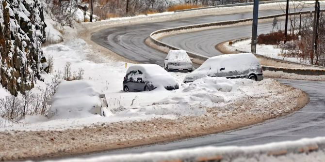 Liegengebliebene und schneebedeckte Autos stehen auf und neben einer Strasse.