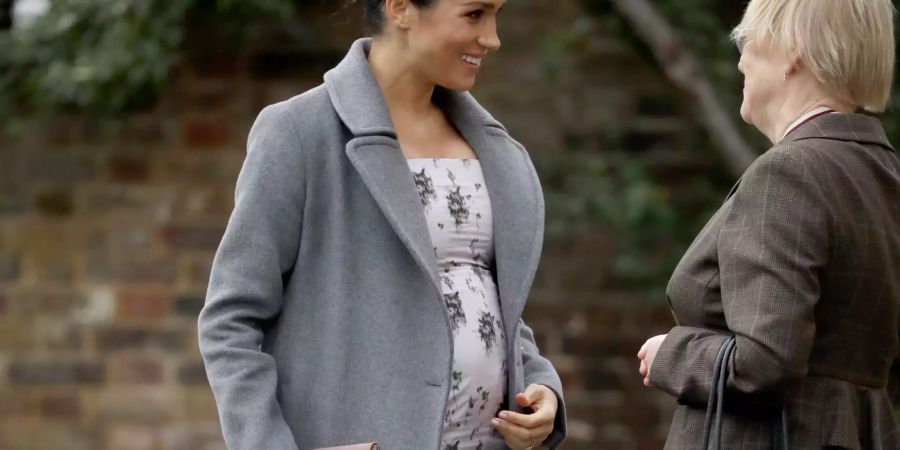 Meghan Markle zeigt ihren wachsenden Babybauch in einem weissen Blumenkleid.