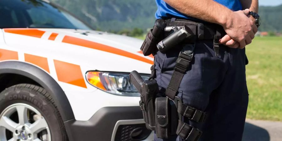 Ein Polizist der Kantonspolizei Glarus steht vor einem Polizeiauto.