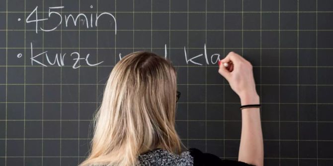 Eine Lehrerin schreibt etwas an die Tafel.