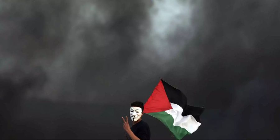 Ein palästinensischer Demonstrant mit einer Guy-Fawkes-Maske zeigt das Victory-Zeichen und hält eine Fahne von Palästina. Die Proteste im Gazastreifen sollen bis zum 15.05. dauern. Anlass sind die Feiern zum 70. Jahrestag der Gründung Israels.