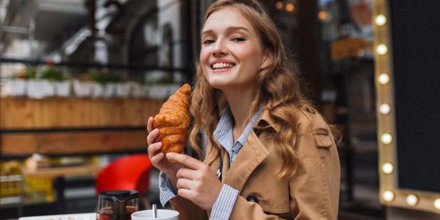 Eine schöne glückliche Frau isst im Bistro ein Croissant.