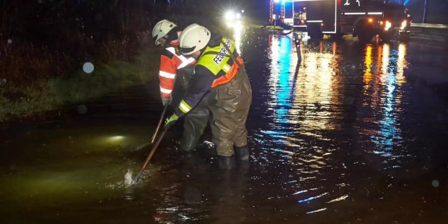 Feuerwehrleute versuchen nach einem Unwetter, mit Pumpen die überflutete Landesstrasse 327 bei Montabaur wieder befahrbar zu machen. Foto: Thomas Frey