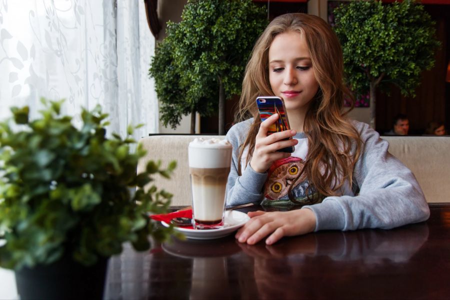 frau schaut auf handy, in café