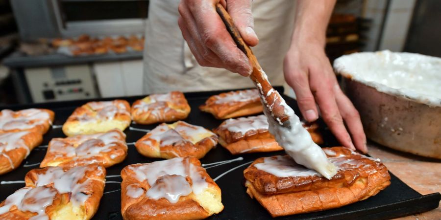 Ein Bäckermeister pinselt Zuckerguss auf süsses Gebäck in seiner Backstube.