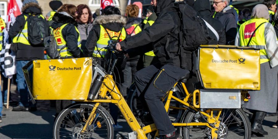 Ein Postbote radelt in Bielefeld an Streikenden einer Verdi-Aktion vorbei.